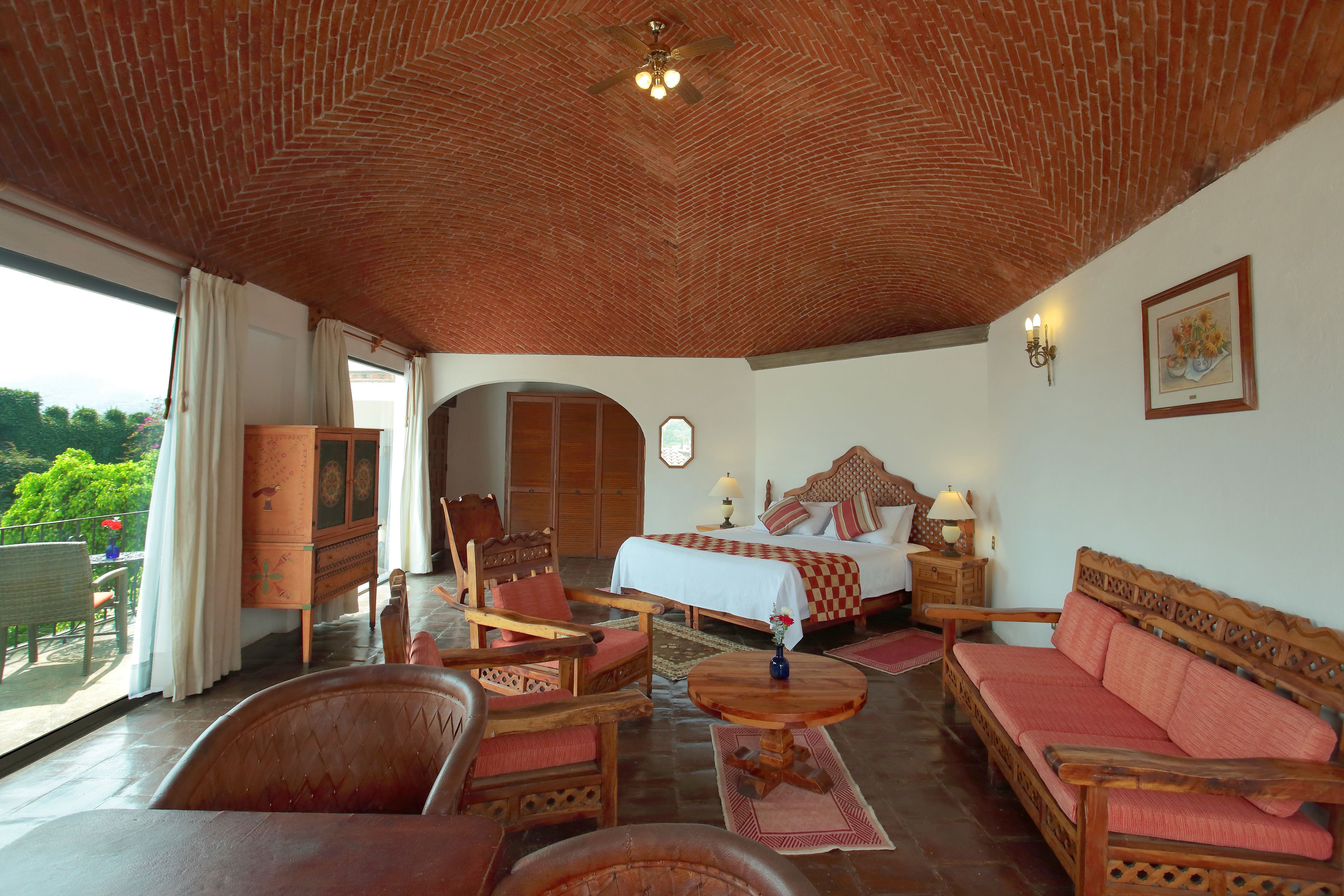 A spacious room with a large bed, wooden furniture, and a balcony with a view of greenery.