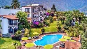 Una villa lujosa con piscina, rodeada de exuberantes jardines y un paisaje montañoso.