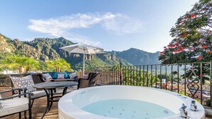 Un jacuzzi en una terraza con mobiliario exterior y vista a las montañas.