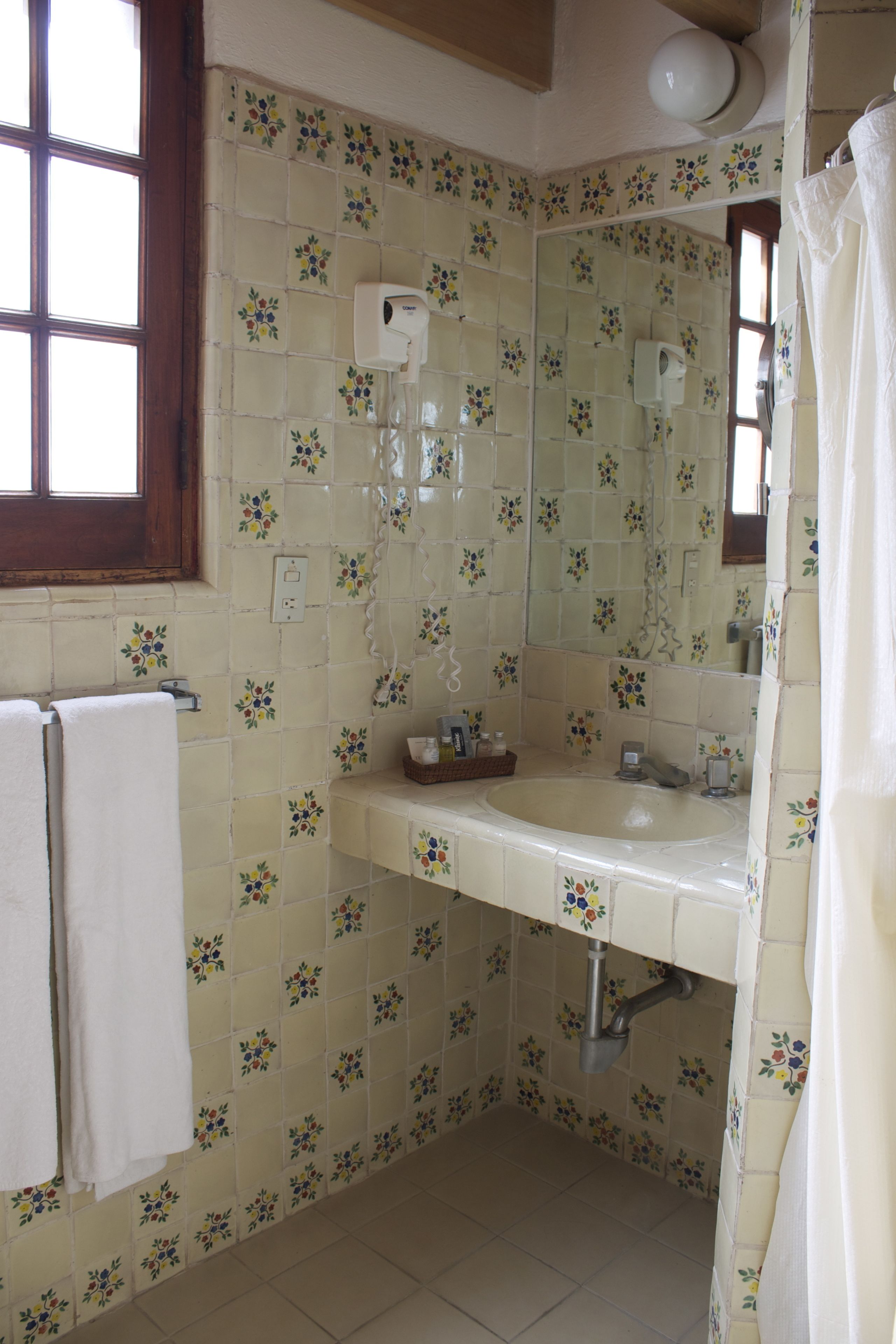 A bathroom with floral tile patterns, a sink, a mirror, and a window.