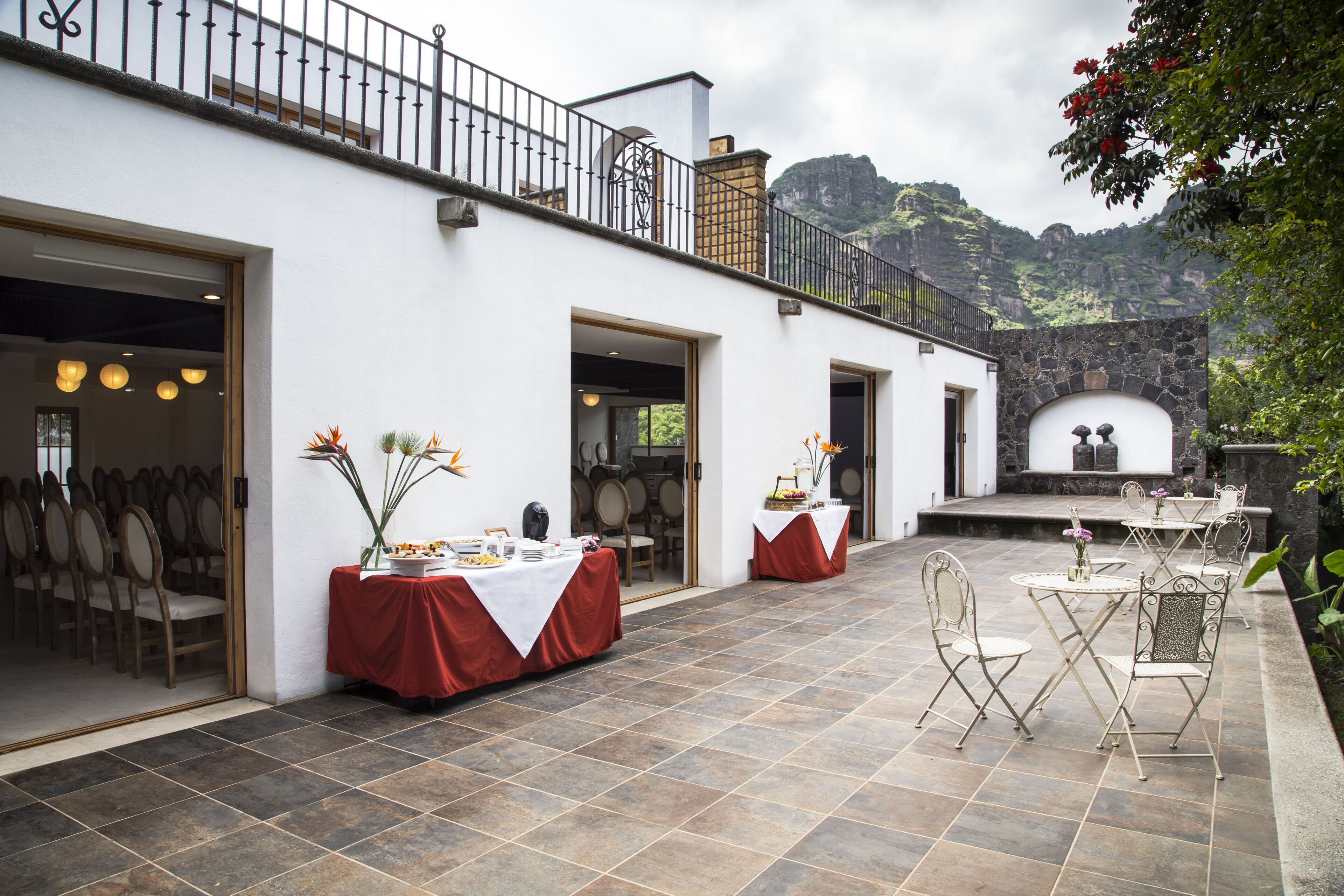 A patio area with tables and chairs, a stone wall, and a view of a mountainous landscape.