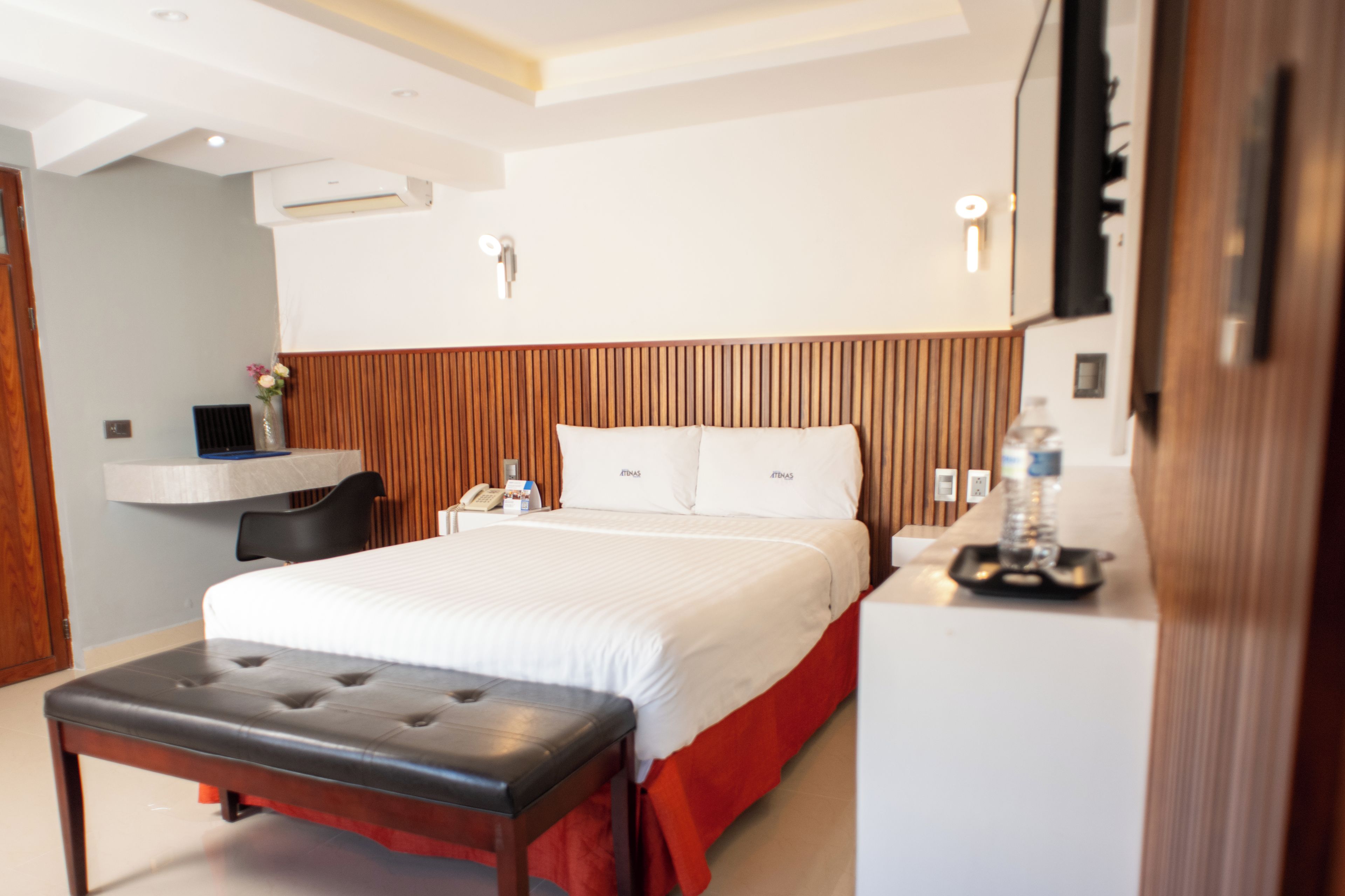 A modern hotel room with a large bed, a desk, and a bench.