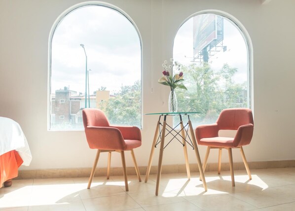 Una habitación con dos sillas rosas, una mesa de vidrio y un jarrón con flores.