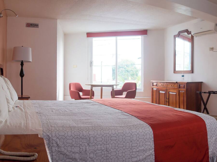 Habitación de hotel con cama, escritorio, silla, televisor y ventana.