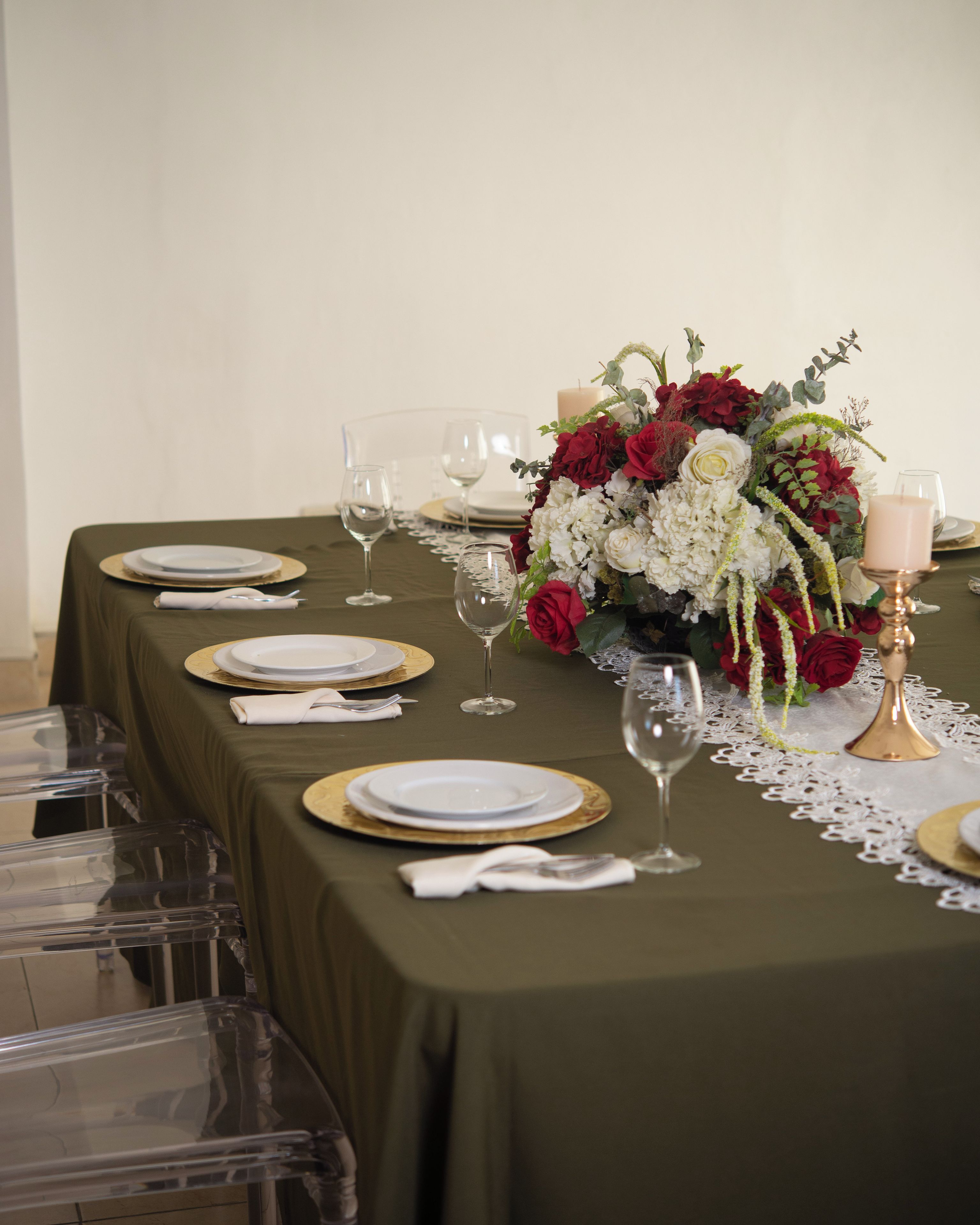 A table set for a formal dinner with clear glassware, gold-rimmed plates, and a centerpiece of red and white flowers.