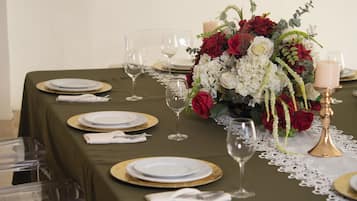 Een gedekte tafel voor een formeel diner, met transparant glaswerk, borden met gouden rand en een bloemenstuk van rode en witte bloemen.