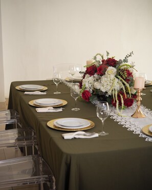 Mesa dispuesta para una cena formal, con cristalería transparente, platos con detalles dorados y un centro de mesa con flores rojas y blancas.