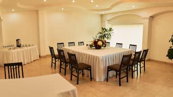 A dining area with a large round table, multiple chairs, a floral centerpiece, and a potted plant.