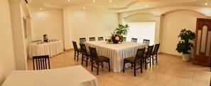 A dining area with a large round table, multiple chairs, a floral centerpiece, and a potted plant. - Hotel Atenas (Xalapa)