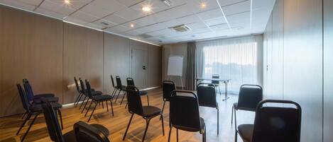 Un salón de conferencias con una pizarra, sillas negras y suelo de madera.