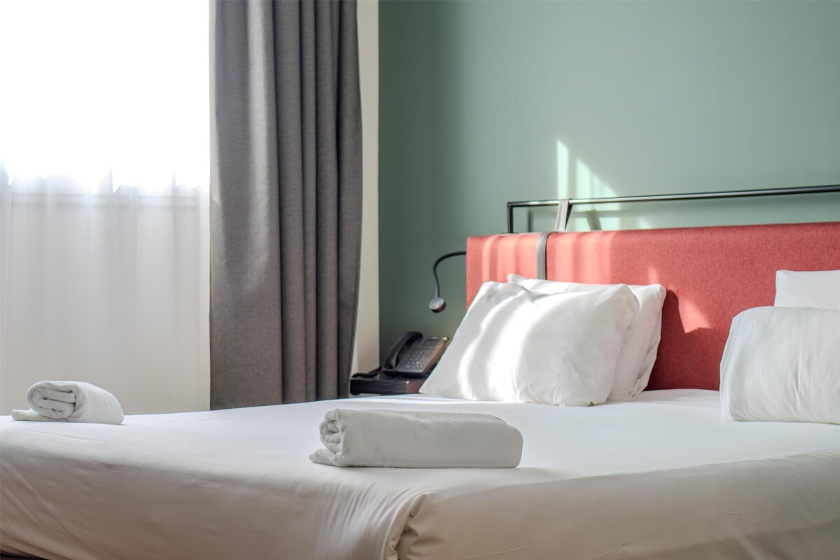 A neatly made bed with white linens, a red headboard, and a telephone on a bedside table.