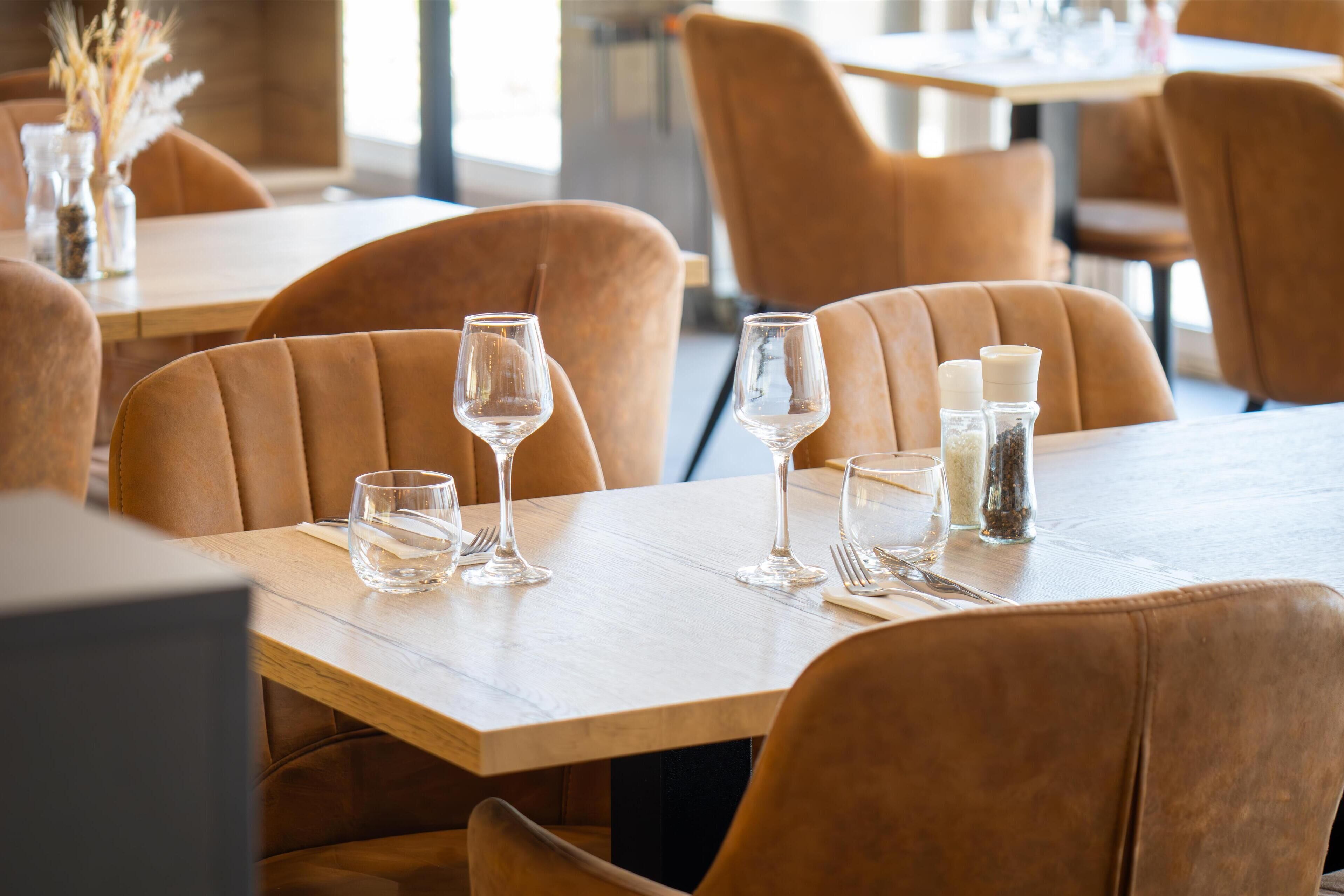 Mesa de comedor servida con copas de vino, vasos de agua y saleros y pimenteros en un restaurante con sillas de cuero.