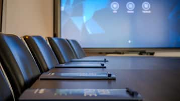 Une salle de conférence avec une longue table, des fauteuils en cuir noir et un écran numérique affichant l’heure.