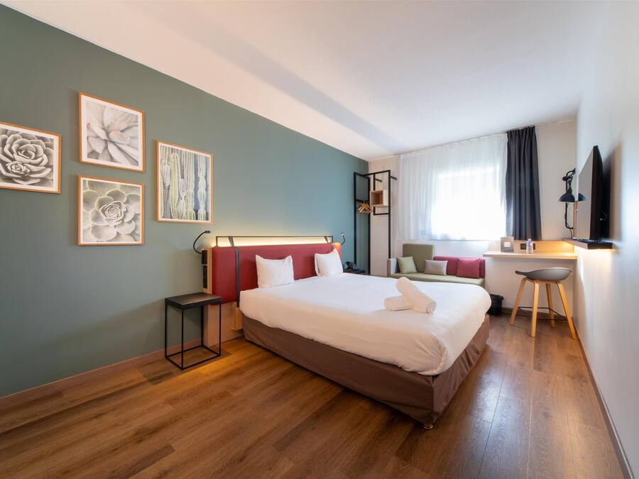 Une chambre d’hôtel comprenant un lit, une table de chevet, un bureau, une chaise et une œuvre d’art au mur.