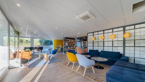 Un interior moderno con un sofá azul, sillas coloridas y una estantería.