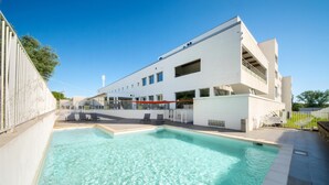 Un edificio moderno con piscina, asientos al aire libre y un cielo azul despejado.