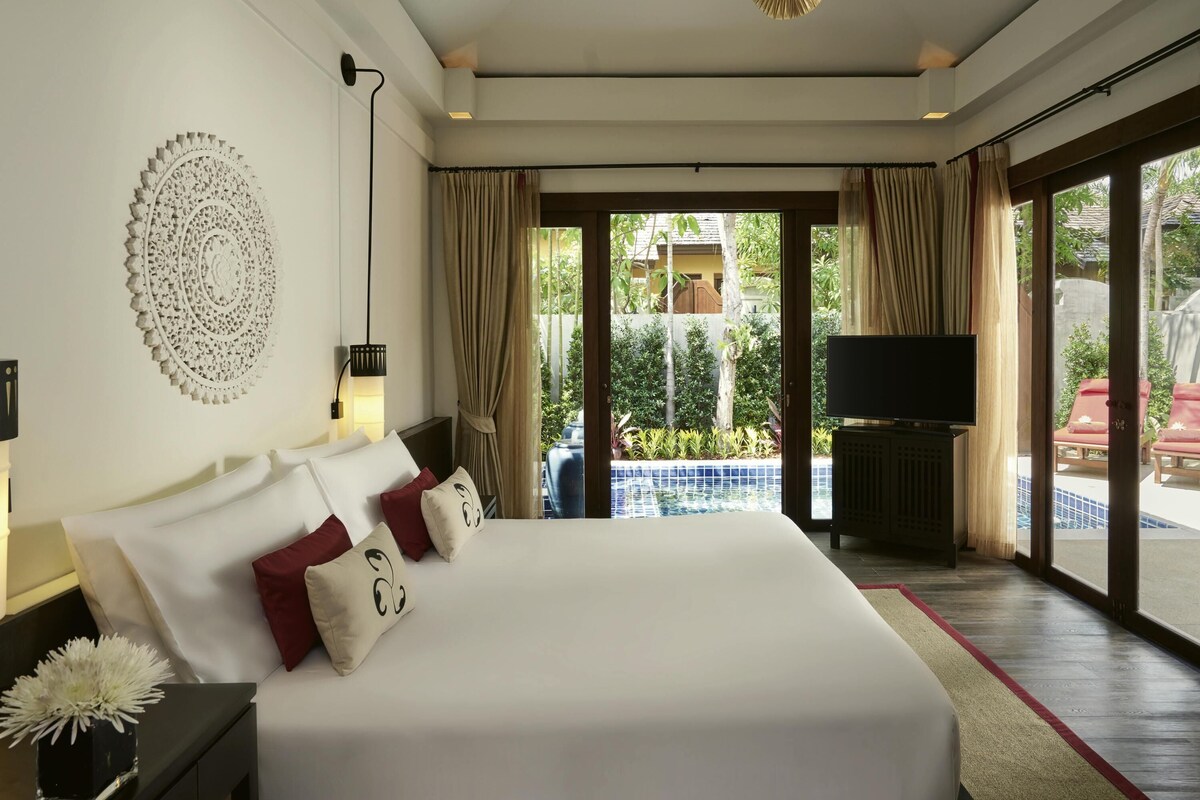 A spacious bedroom with a large bed, a ceiling fan, a TV, and a view of a pool and outdoor area.