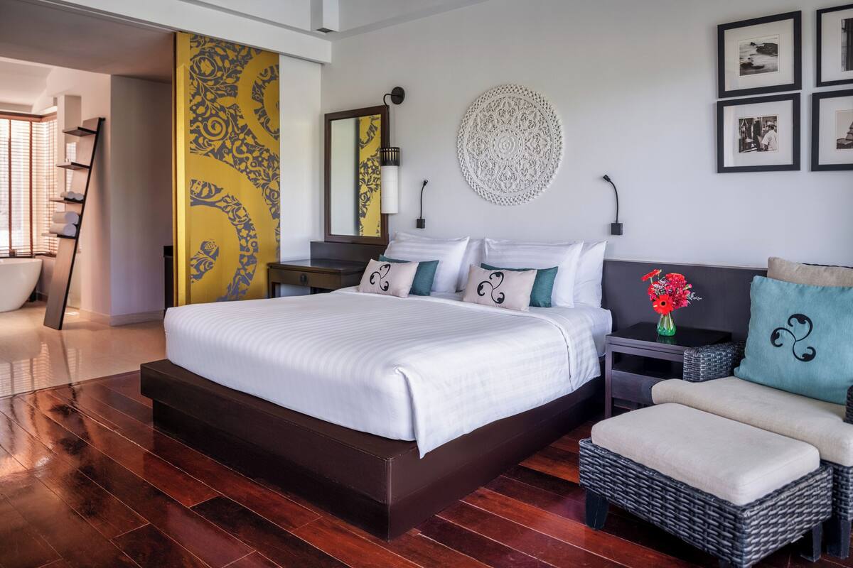 A modern bedroom with a large bed, a nightstand, a wicker chair, and a decorative wall piece.