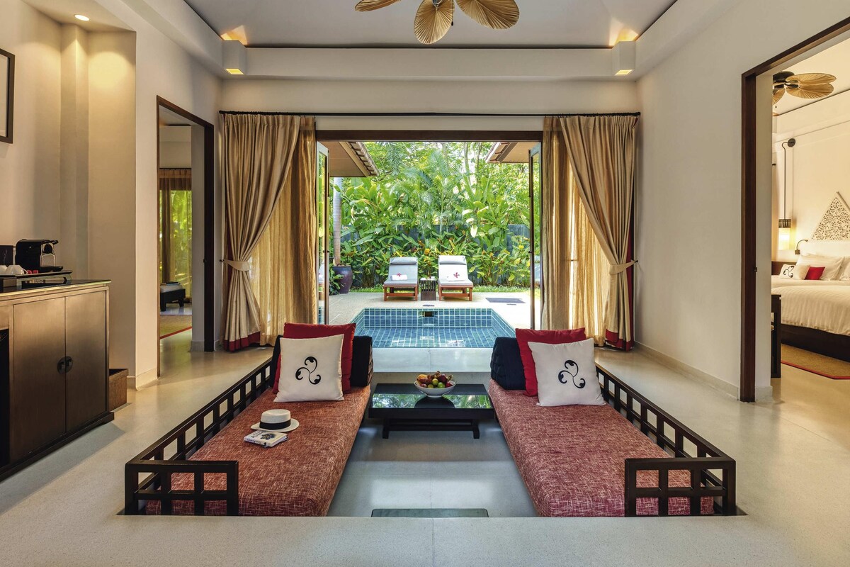 A spacious room with a large bed, a dining table, and a view of a lush garden.