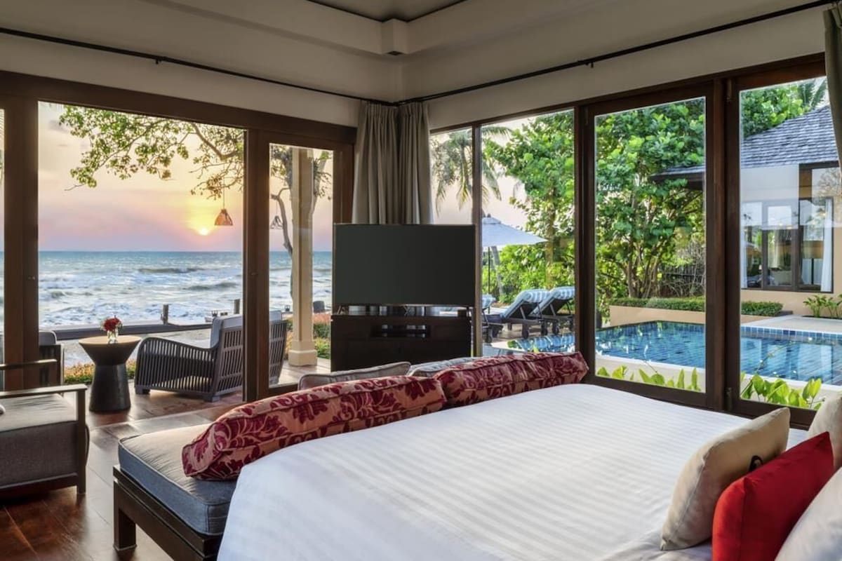 A bedroom with a large bed, a TV, and a view of the ocean and pool.
