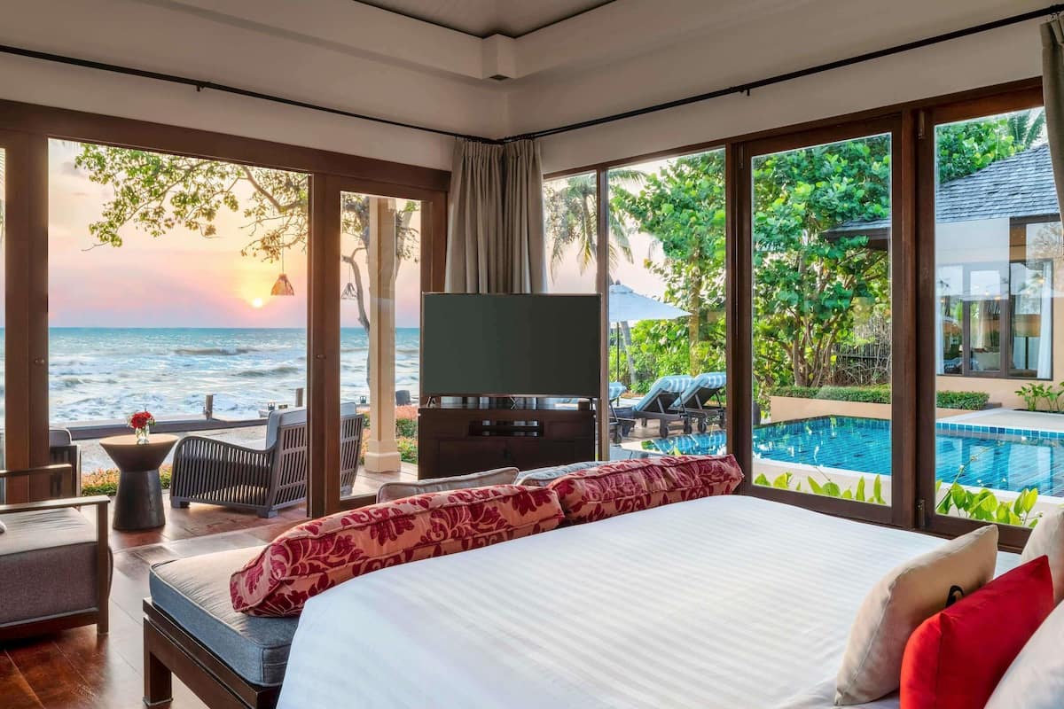 Une chambre avec un grand lit, une télévision, une vue sur l’océan et une piscine.