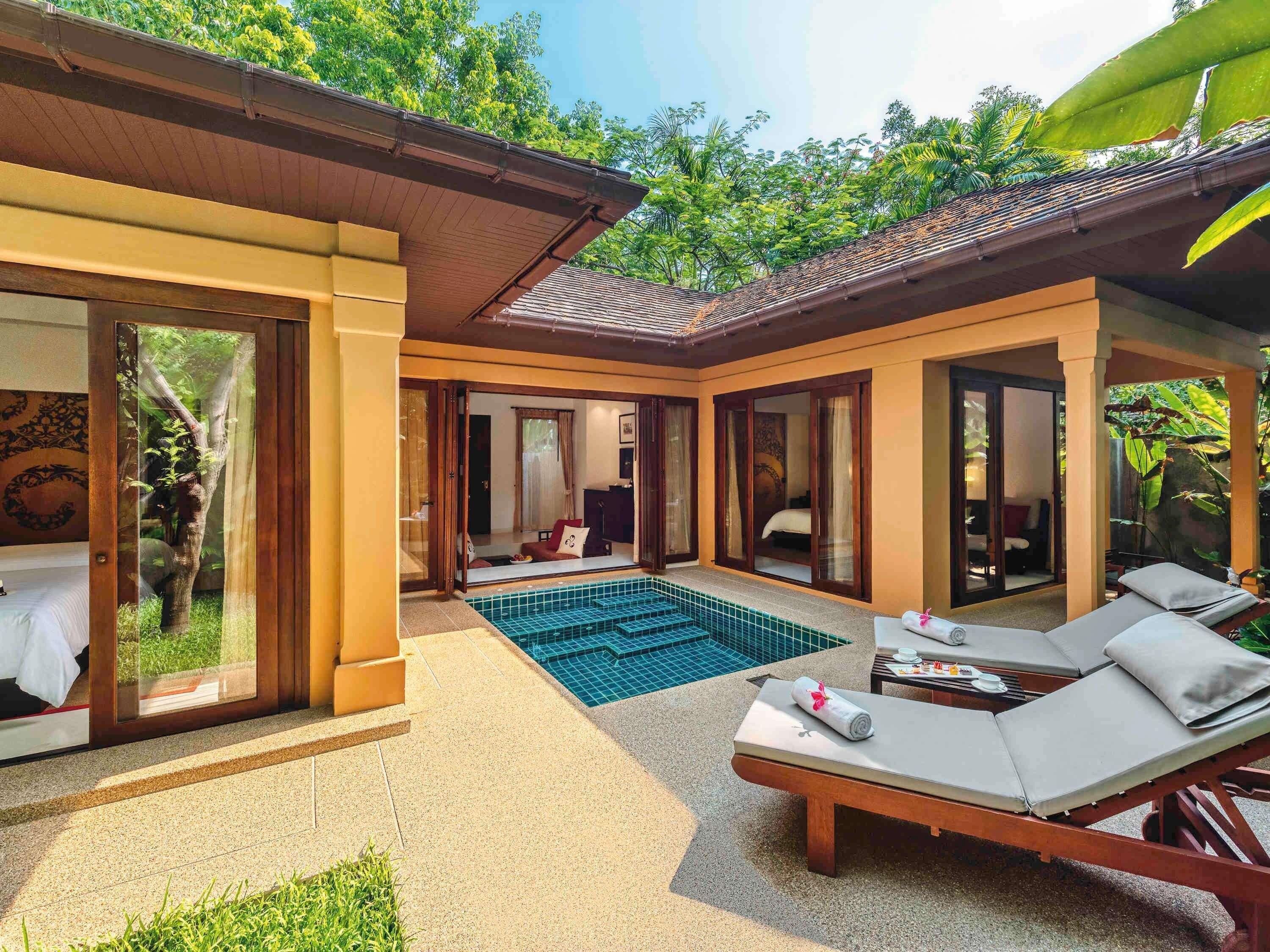 A hotel suite with a private pool, a sitting area with a table and chairs, and a bedroom with a large window.