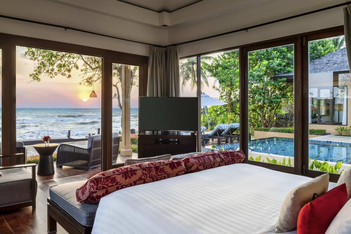 A bedroom with a large bed, a TV, and a view of the ocean and pool.