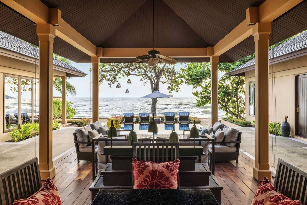 A covered outdoor seating area with a view of the ocean, featuring a table, chairs, and a ceiling fan.