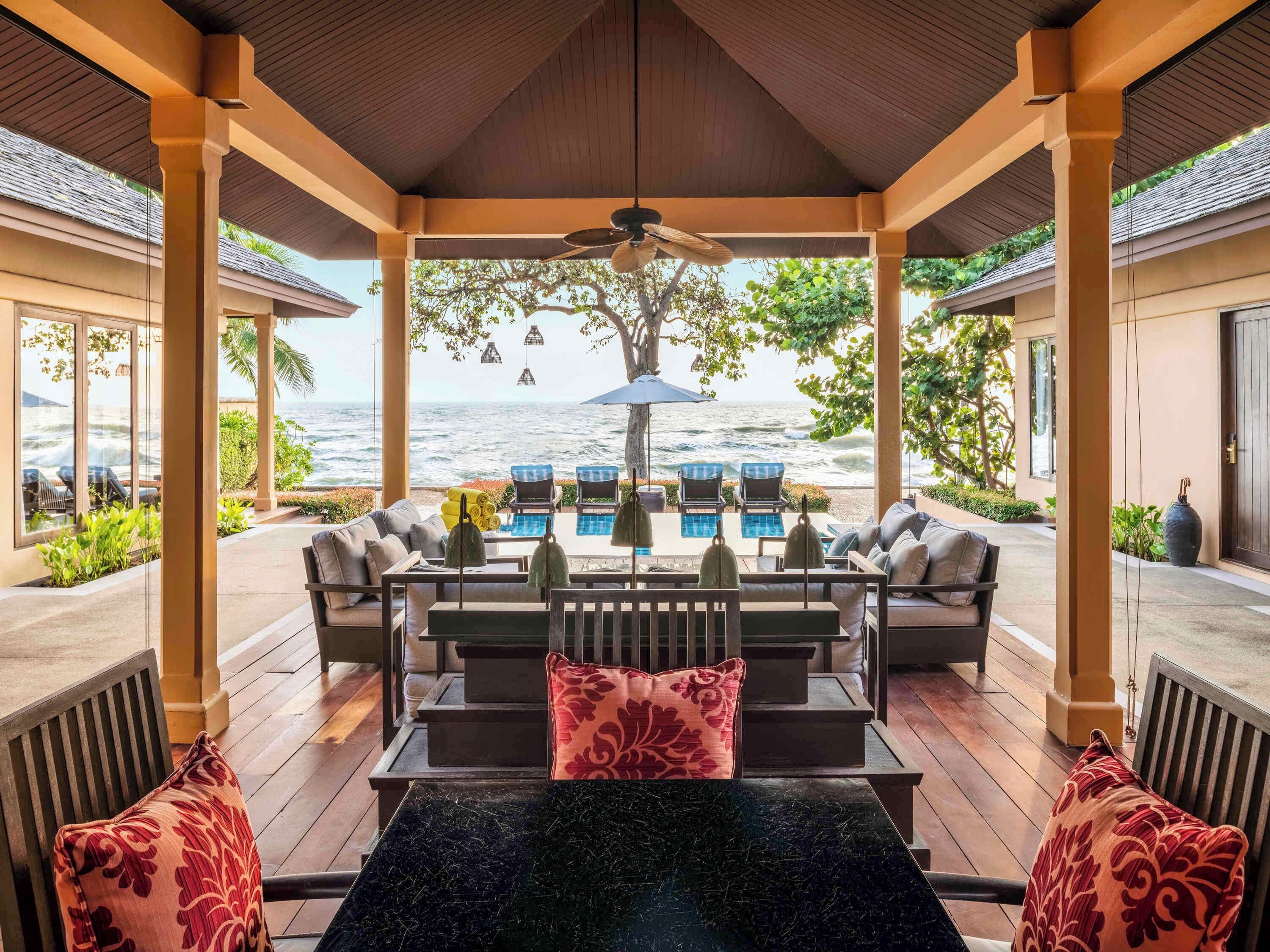 Een overdekt terras met een zwembad, ligstoelen en uitzicht op de oceaan.