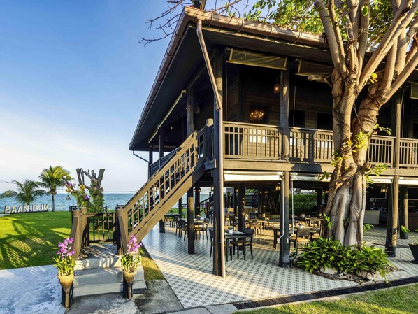 A two-story building with a balcony, outdoor seating, and a view of the sea.