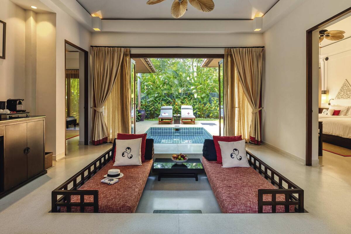 A spacious room with a large bed, a dining table, and a view of a lush garden.