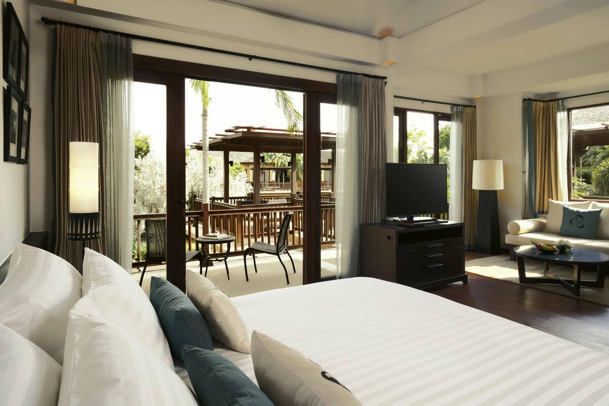 A hotel room with a large bed, a TV, a sofa, and a balcony with outdoor furniture.