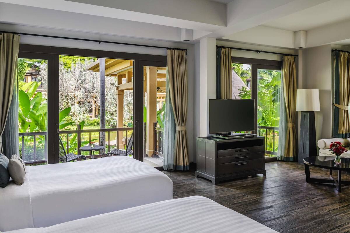 A hotel room with a bed, a TV, a desk, and a view of a garden.