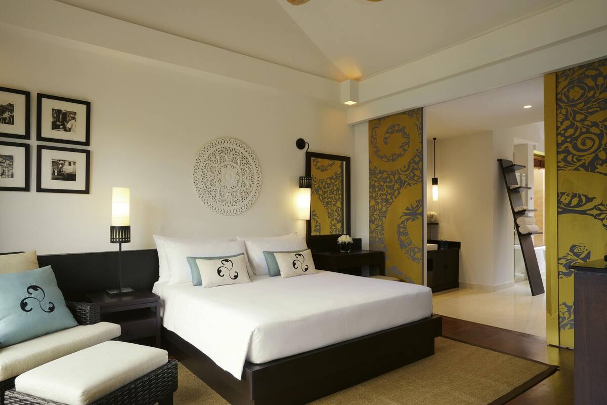 A bedroom with a large bed, a bedside table, a lamp, a chair, and a decorative wall piece.
