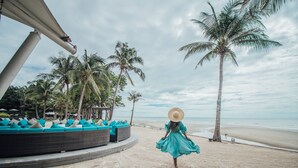 A beach with a lounge area featuring blue cushions and a palm tree in the background. - Mövenpick Asara Resort & Spa Hua Hin (Hua Hin)