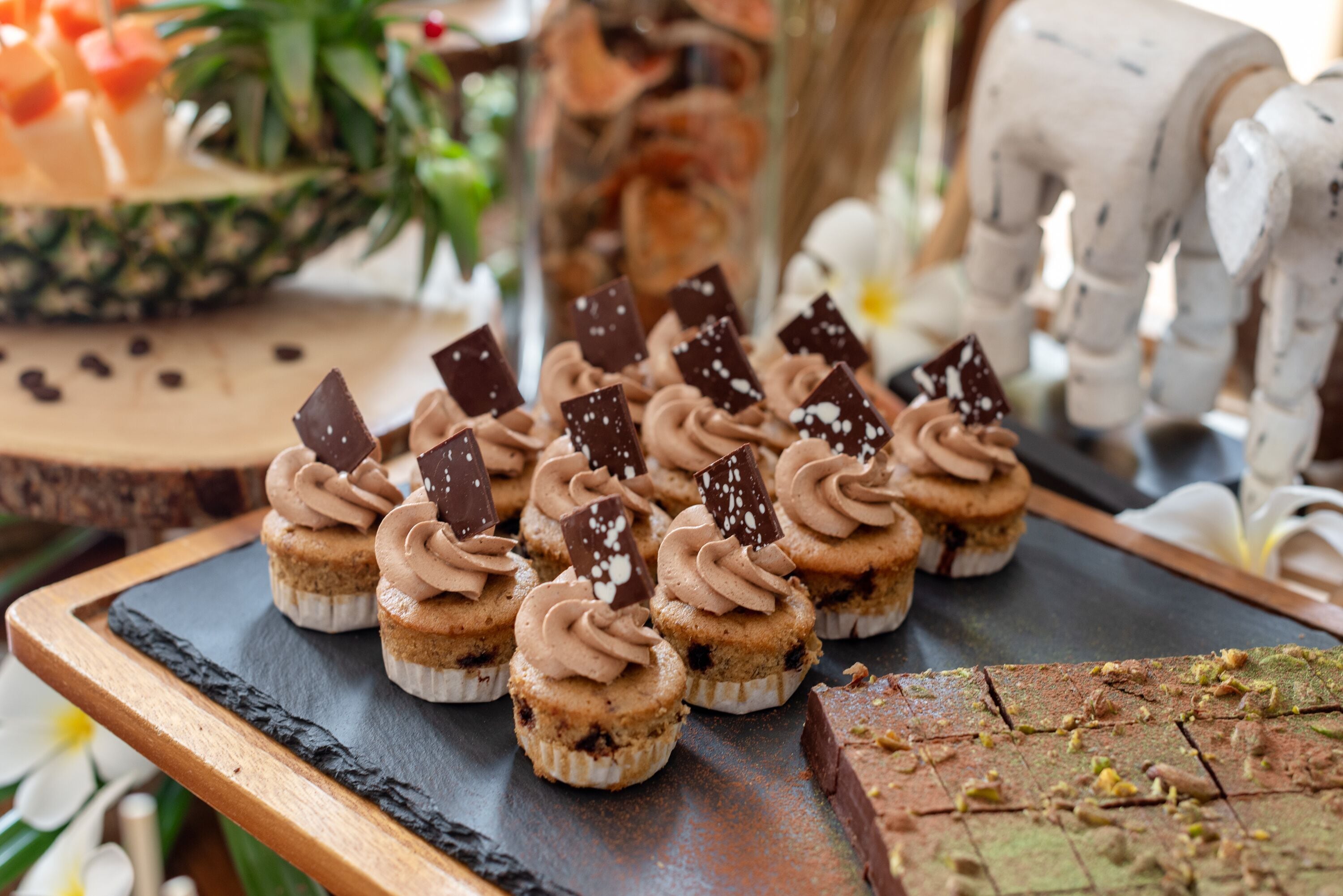 A tray of cupcakes with chocolate frosting and chocolate pieces on a slate board.