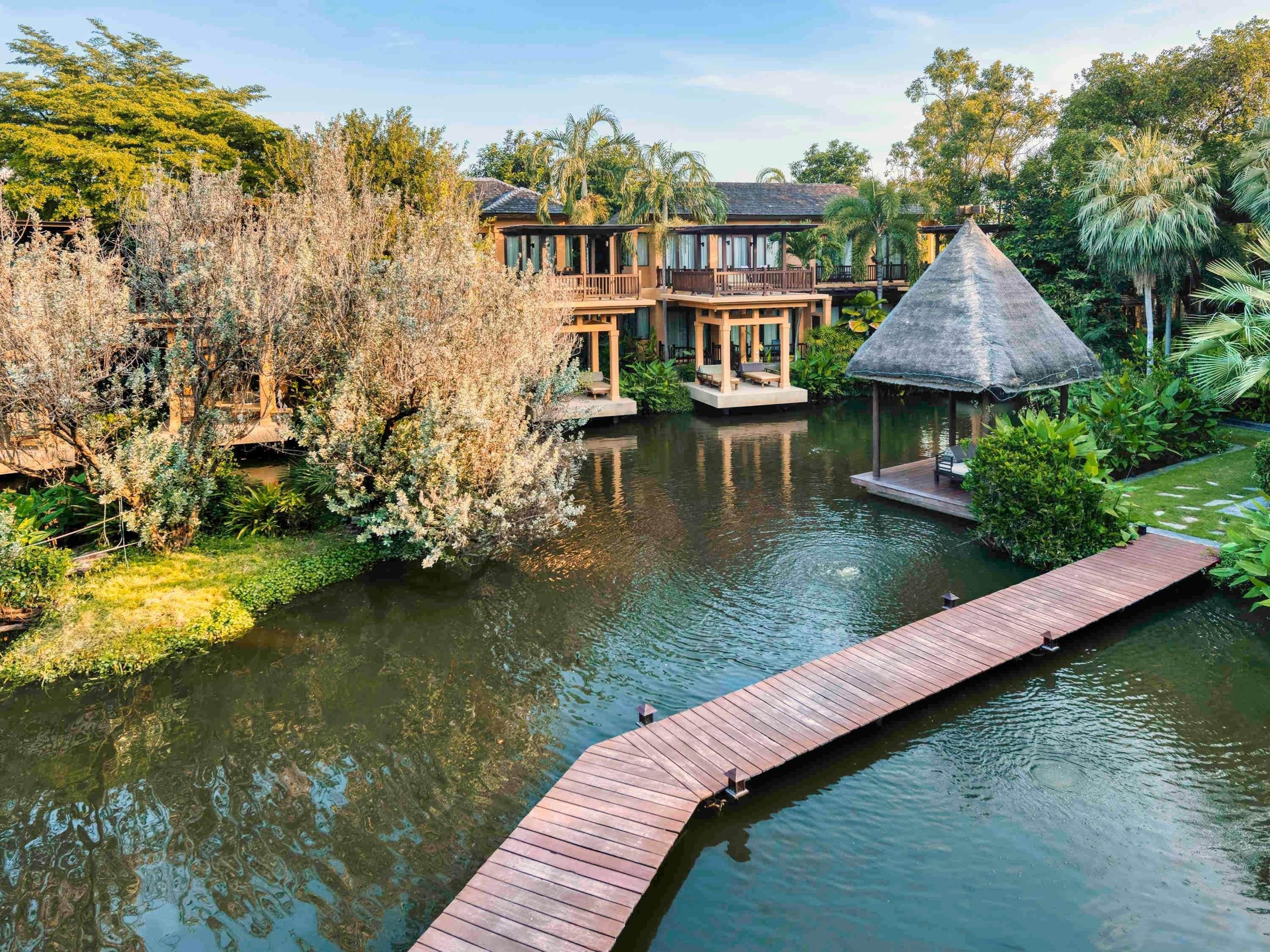 A resort with a water body, wooden deck, and a thatched-roof structure.