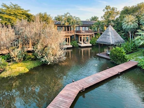 A resort with a water body, wooden deck, and a thatched-roof structure.
