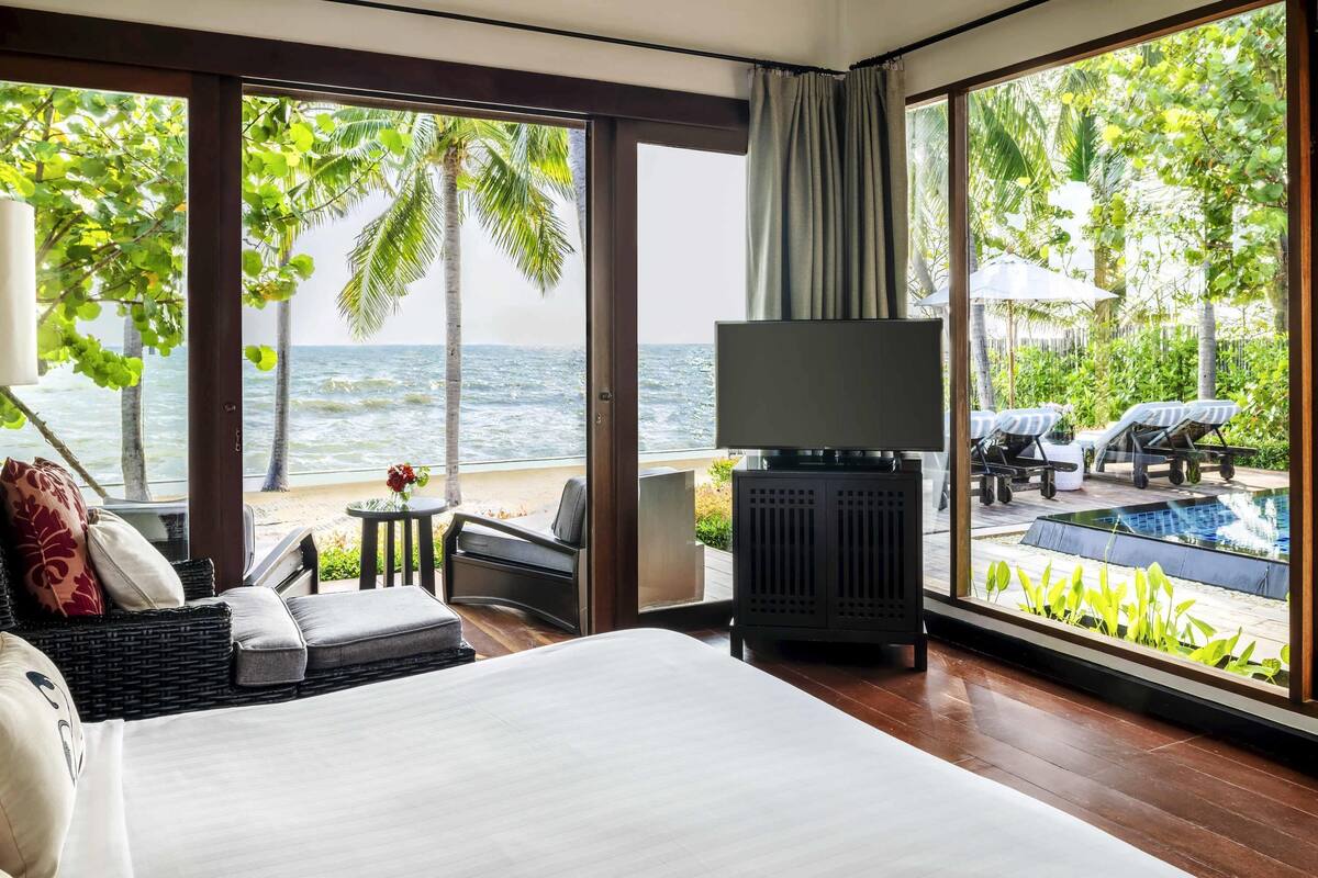 A bedroom with a large bed, a TV, and a view of the ocean and pool area.