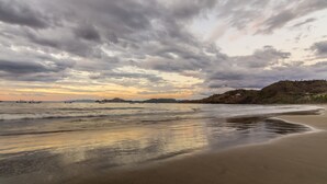 Una playa con un mar tranquilo, barcos a lo lejos y un cielo nublado.