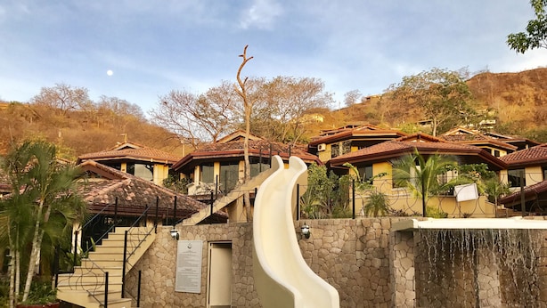 Zona de piscina con tobogán de agua, pared de piedra y vistas a casas con tejados rojos.