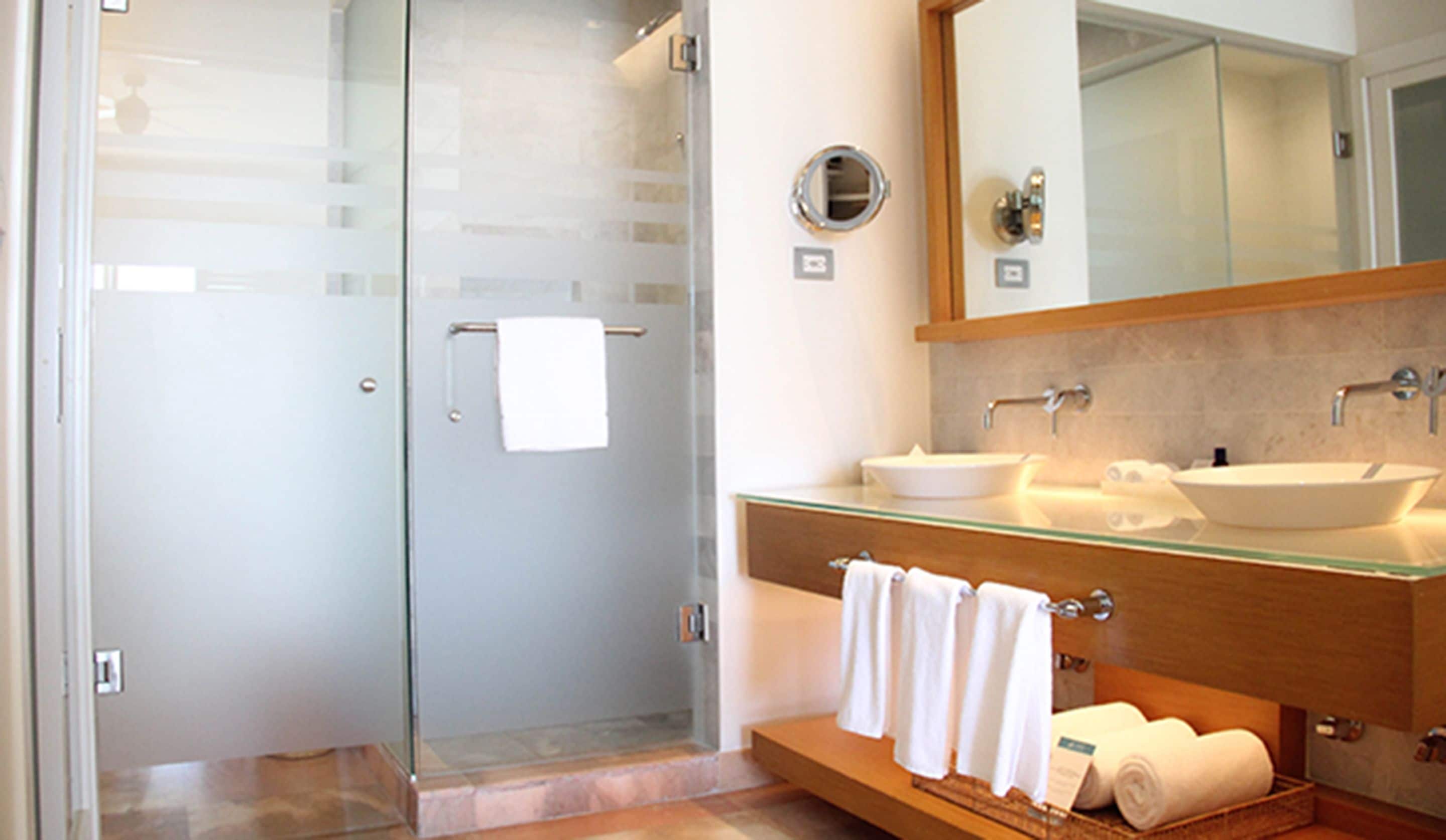 Un baño moderno con cabina de ducha de vidrio, dos lavamanos, un espejo grande y un perchero para toallas.