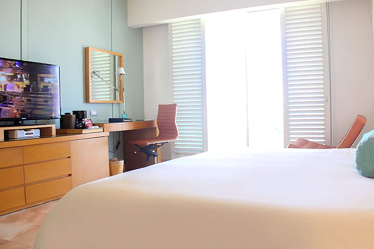 A hotel room with a bed, a desk, a chair, a television, and a window with blinds.