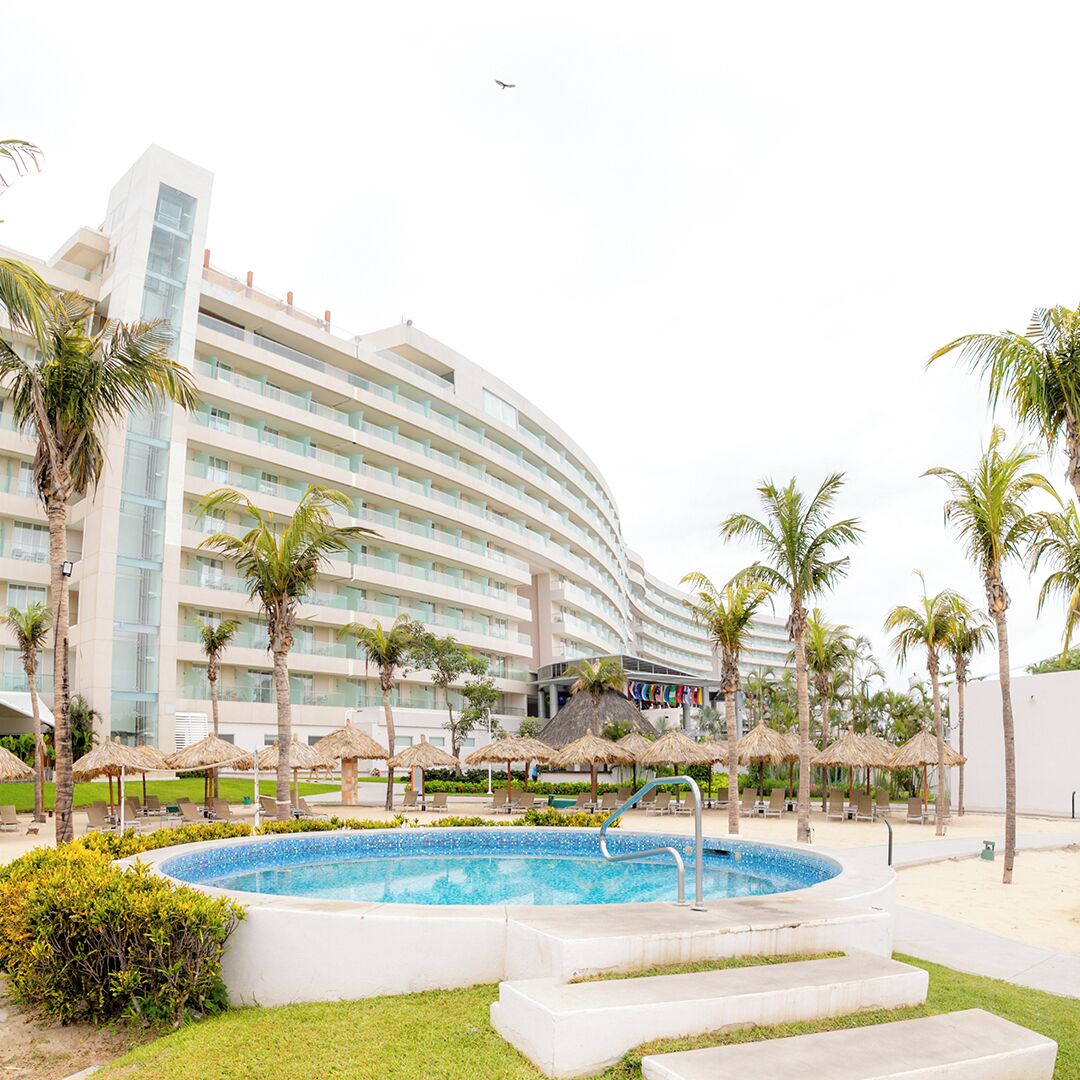 Un hôtel moderne doté d’une grande piscine, de palmiers et de parasols de plage.