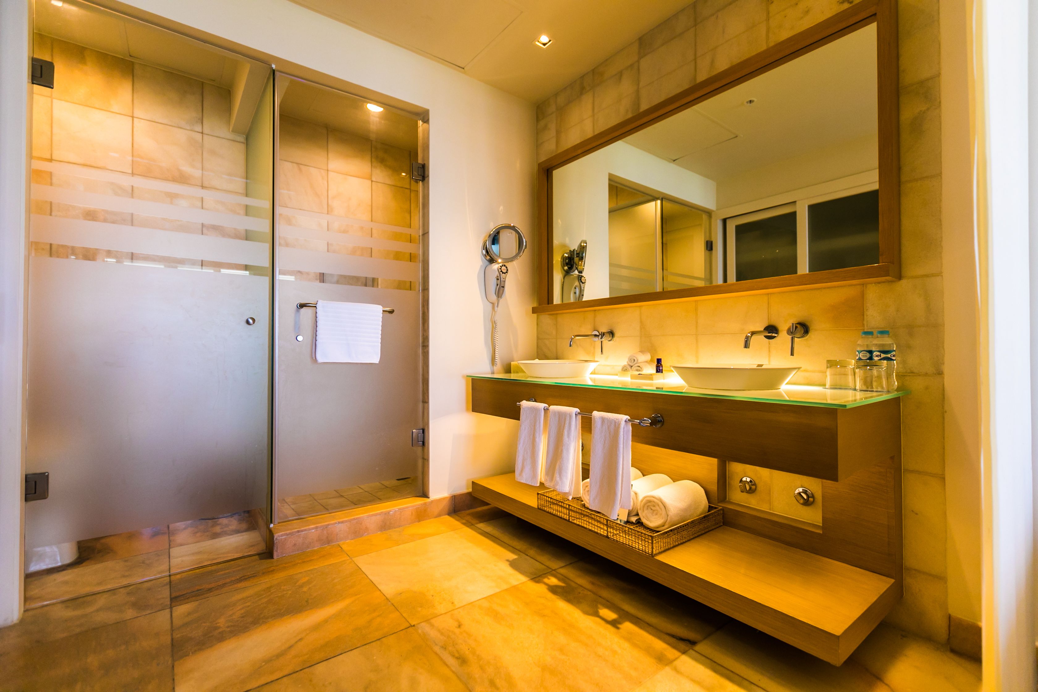 Une salle de bain moderne dotée d’une douche à parois de verre, d’un grand miroir et d’un meuble-lavabo avec un plan de travail en verre.