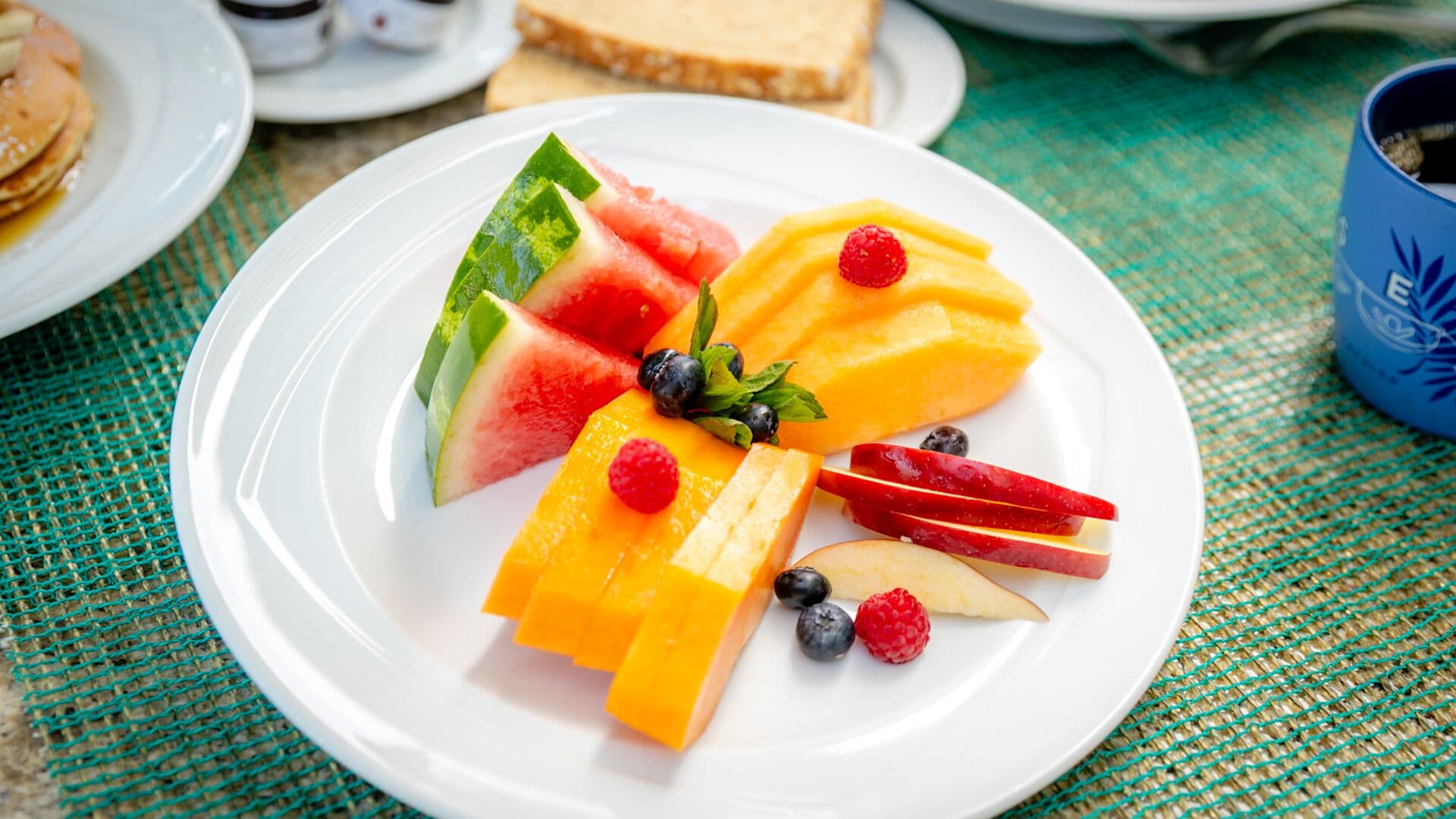 A plate of fruit including watermelon, mango, blueberries, raspberries, and apple slices.