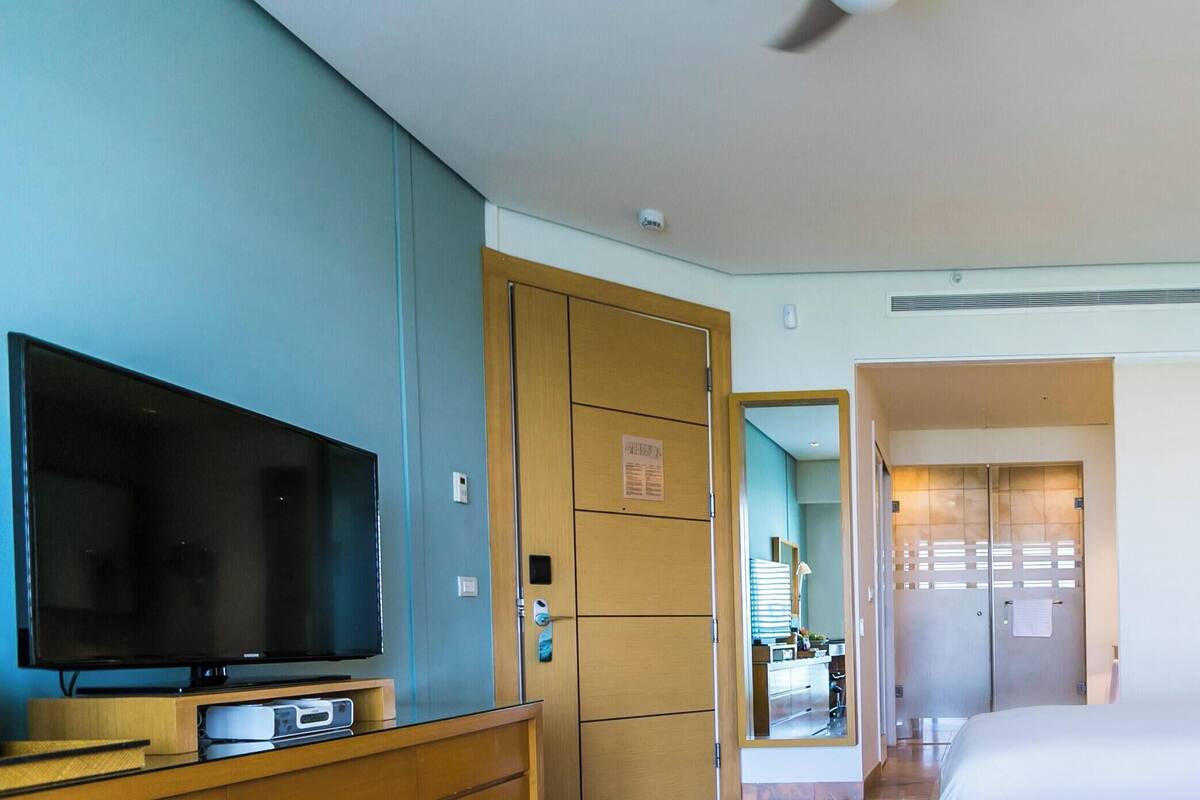 A hotel room with a television, a bed with pillows, a bedside table with a lamp, and a phone.