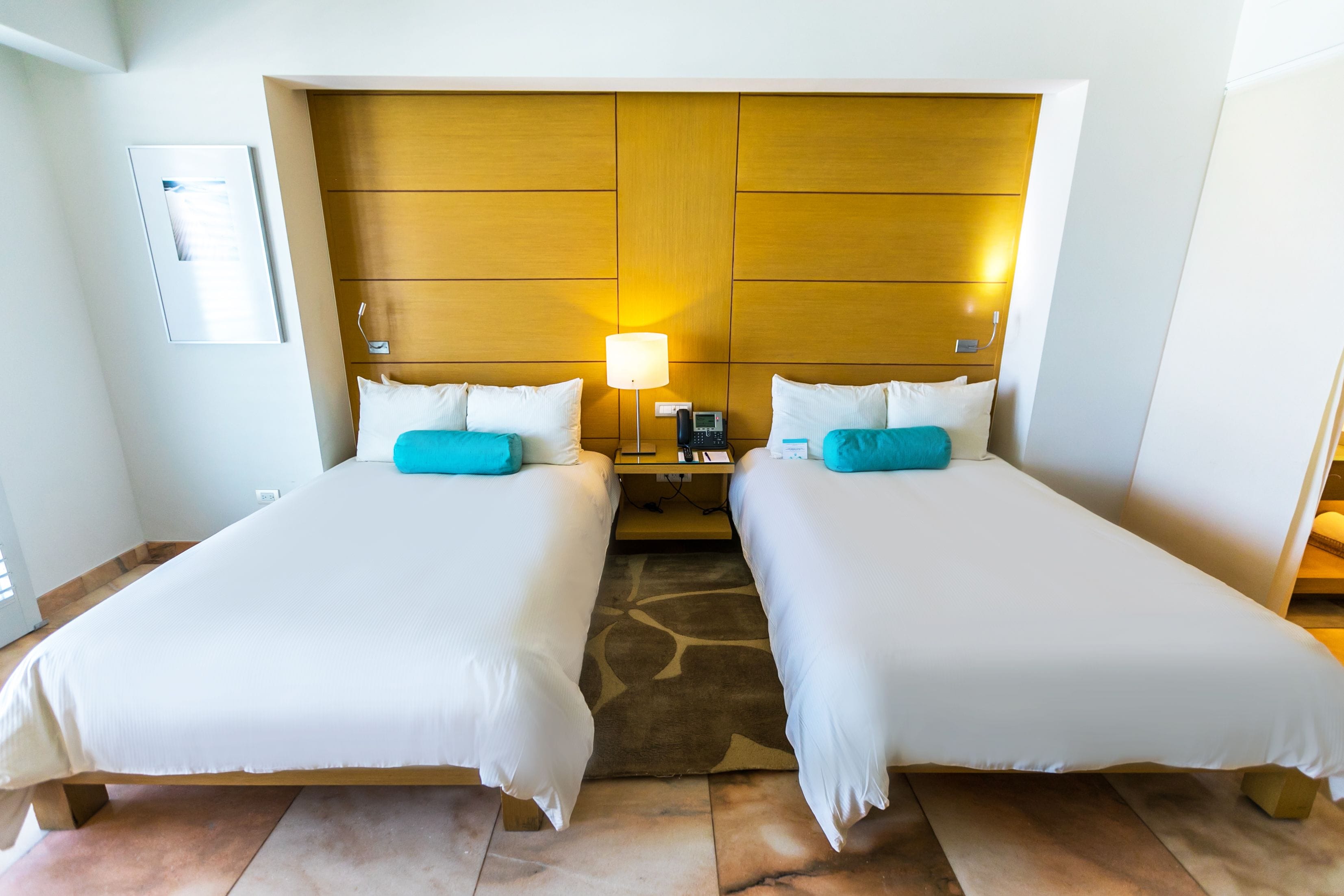 A hotel room with two single beds, a wooden headboard, a nightstand with a lamp, and a phone.