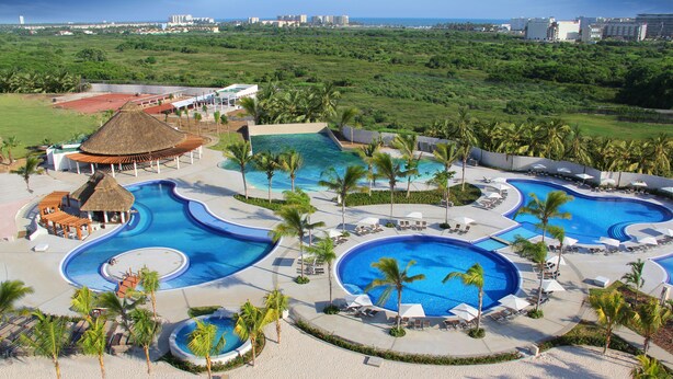 Un complexe hôtelier doté de plusieurs piscines, de palmiers et offrant une vue sur l’océan.