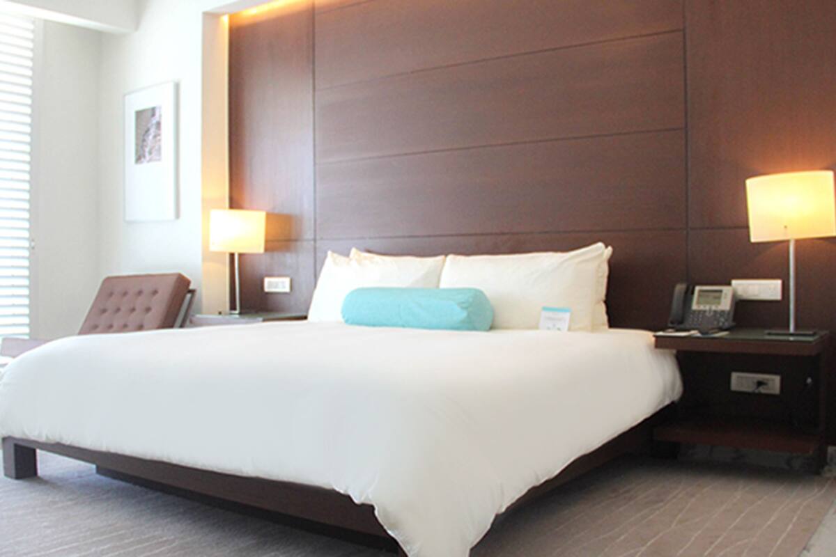 A large bed with white linens, two bedside lamps, a brown headboard, and a chair.